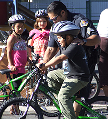 healthy-communities.jpg Police officer helps young boy ride a bike.