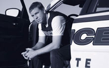 Officer sitting in squad car Officer sitting with legs outside open squad car door.
